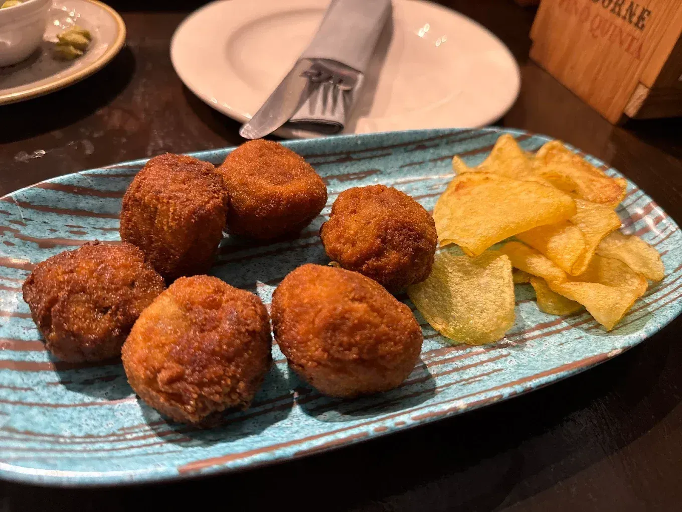 Plato de croquetas doradas y fritas y patatas fritas sobre un plato azul texturizado.