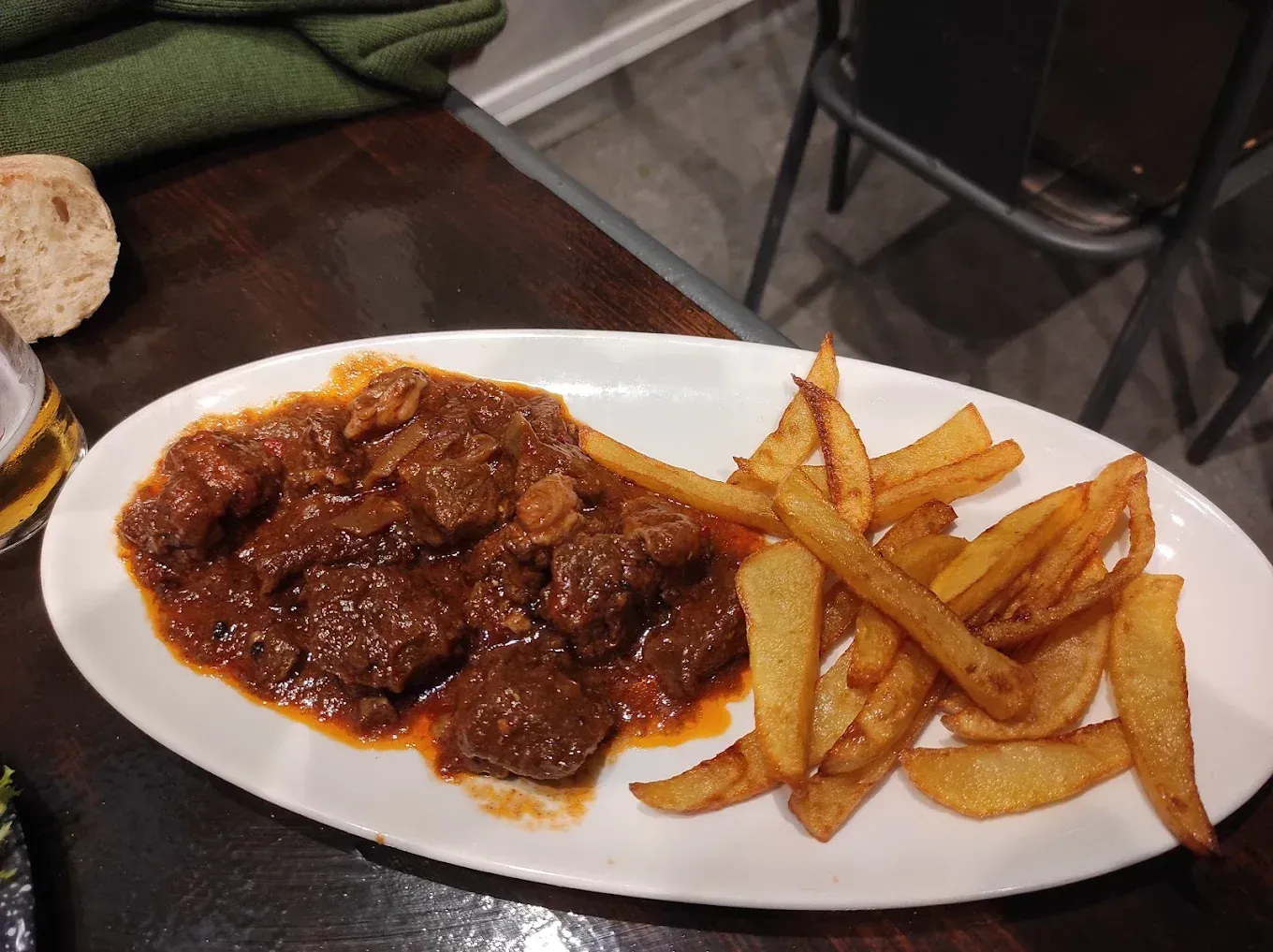 Guiso con patatas fritas en un plato ovalado blanco en una mesa.