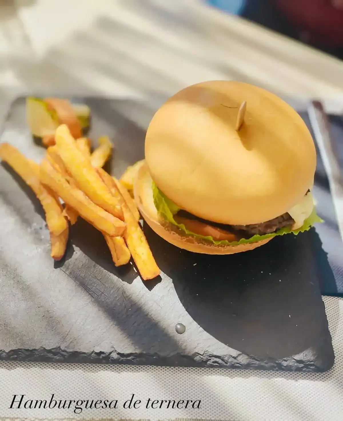 Hamburguesa con patatas fritas y pepinillos sobre pizarra negra.