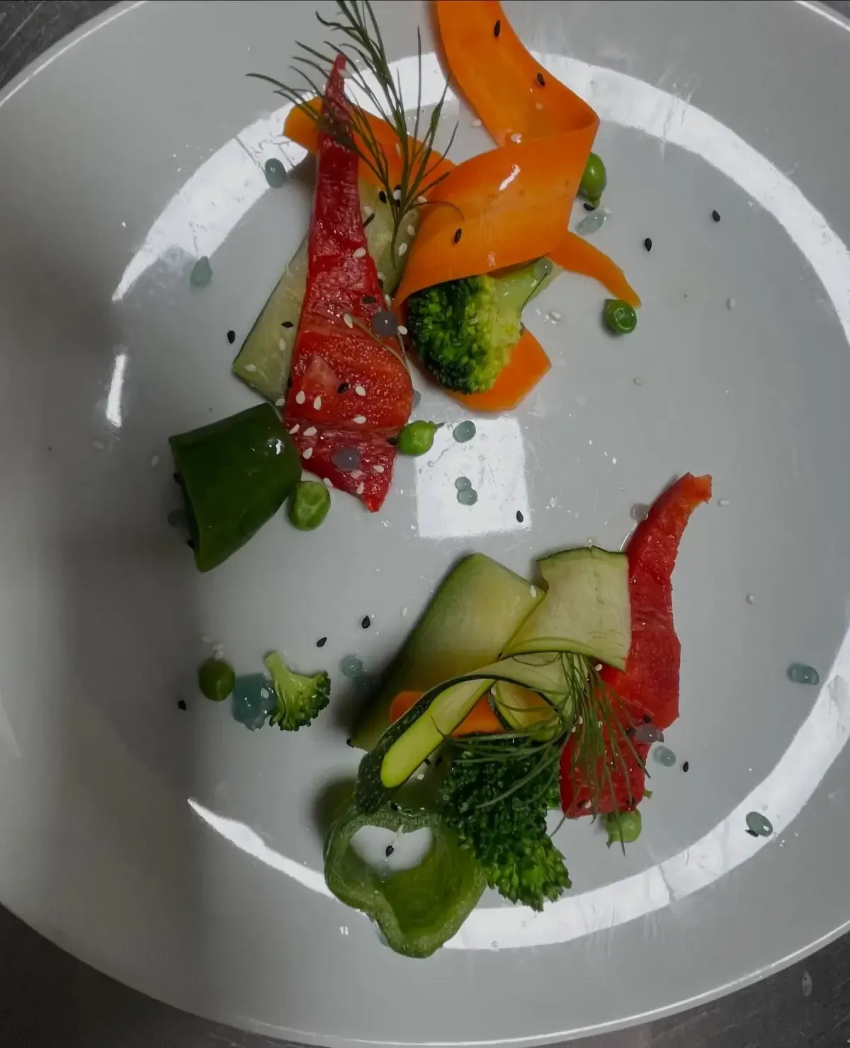 Disposición de verduras coloridas, incluidos pimientos rojos, brócoli y zanahorias, en un plato blanco con eneldo.