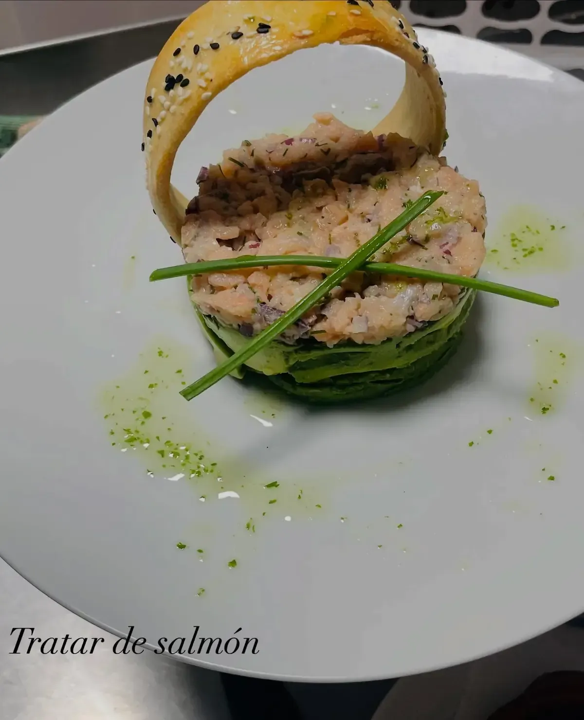 Tartar de salmón con aguacate, hierbas y hojaldre en plato blanco.