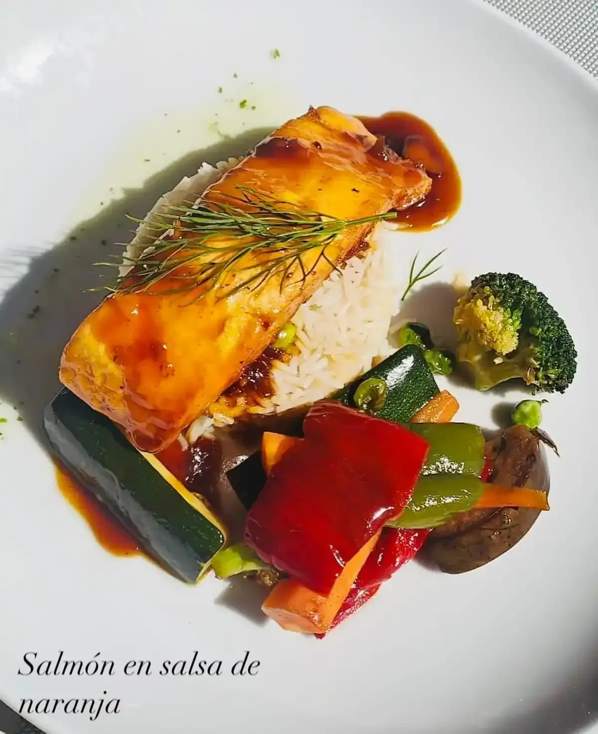 Filete de salmón con salsa de naranja sobre arroz, rodeado de coloridas verduras salteadas.