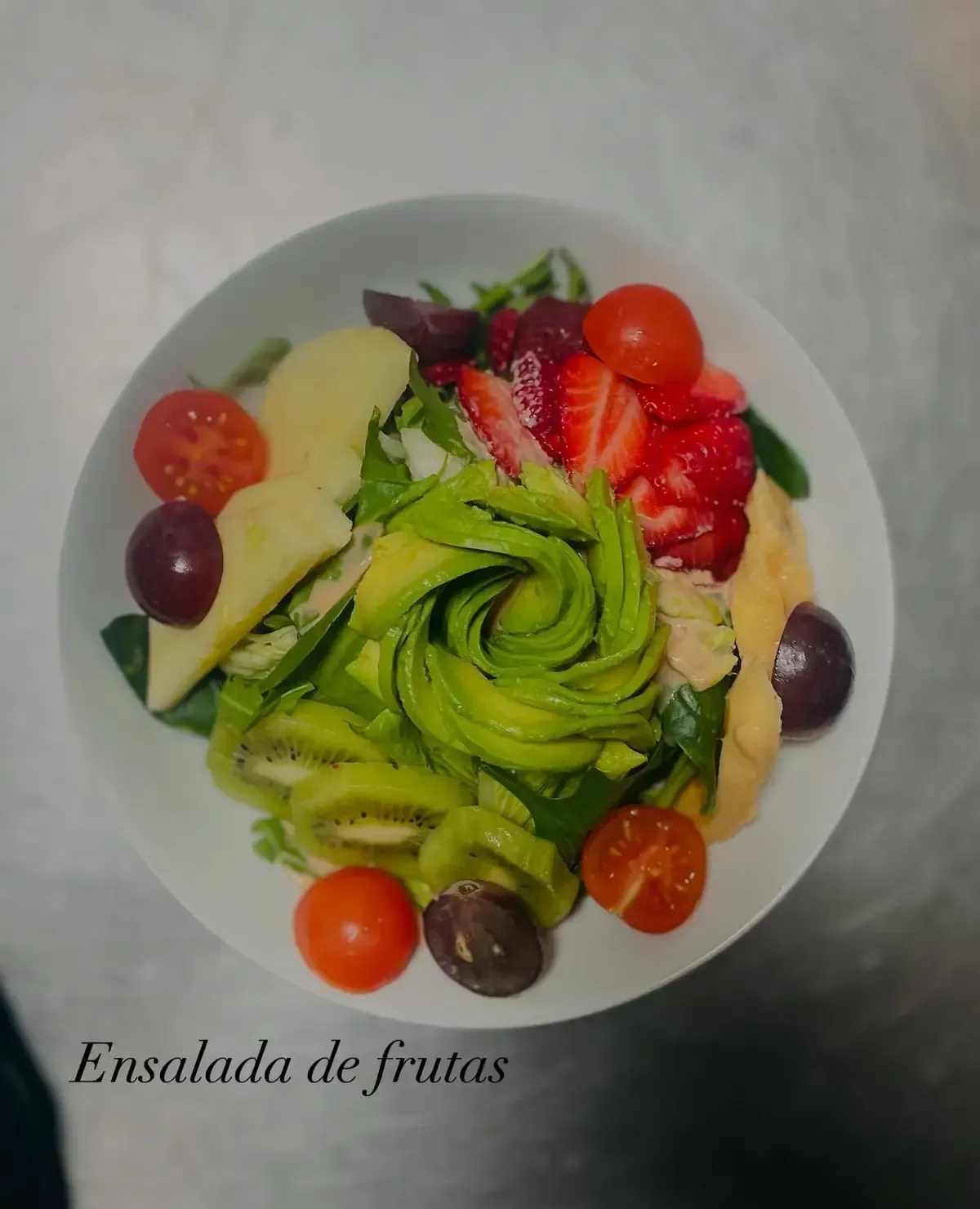 Ensalada de frutas en un tazón blanco con aguacate, kiwi, fresas y uvas.