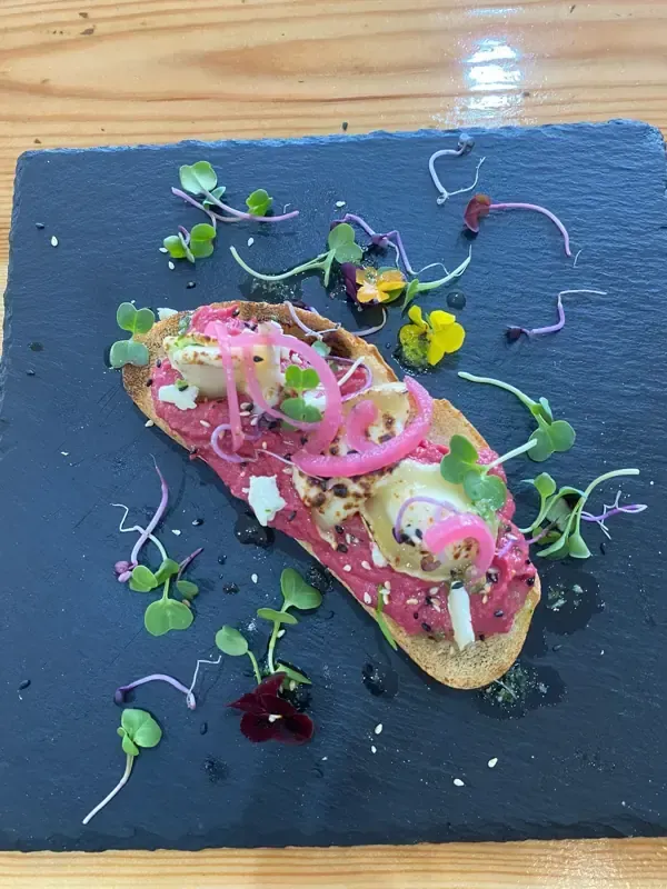 Tostada cubierta con pasta de remolacha rosa, cebollas encurtidas, microvegetales y flores comestibles