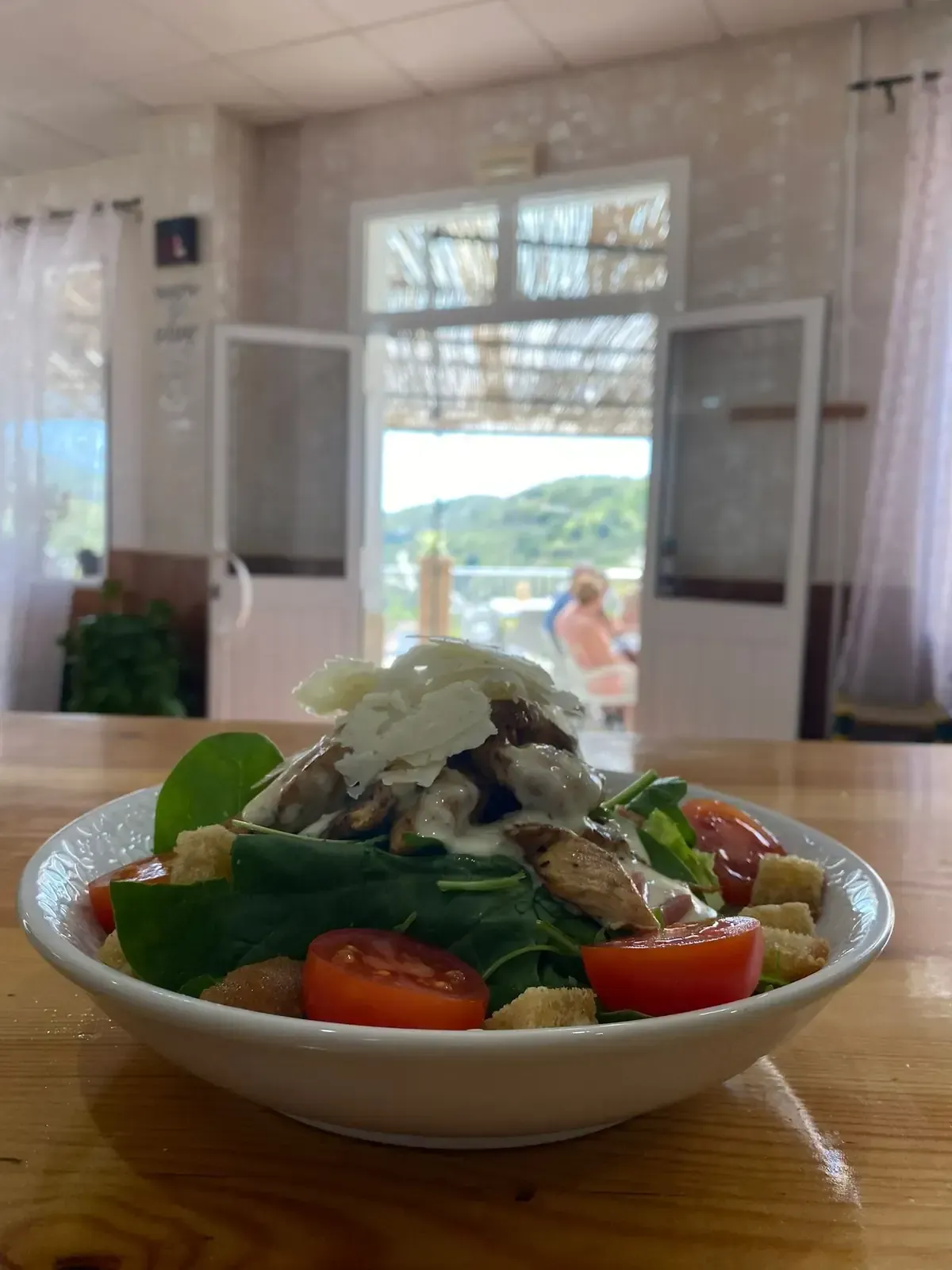 Ensalada en un recipiente blanco sobre la mesa; tomates, crutones y verduras; visión borrosa de puertas abiertas