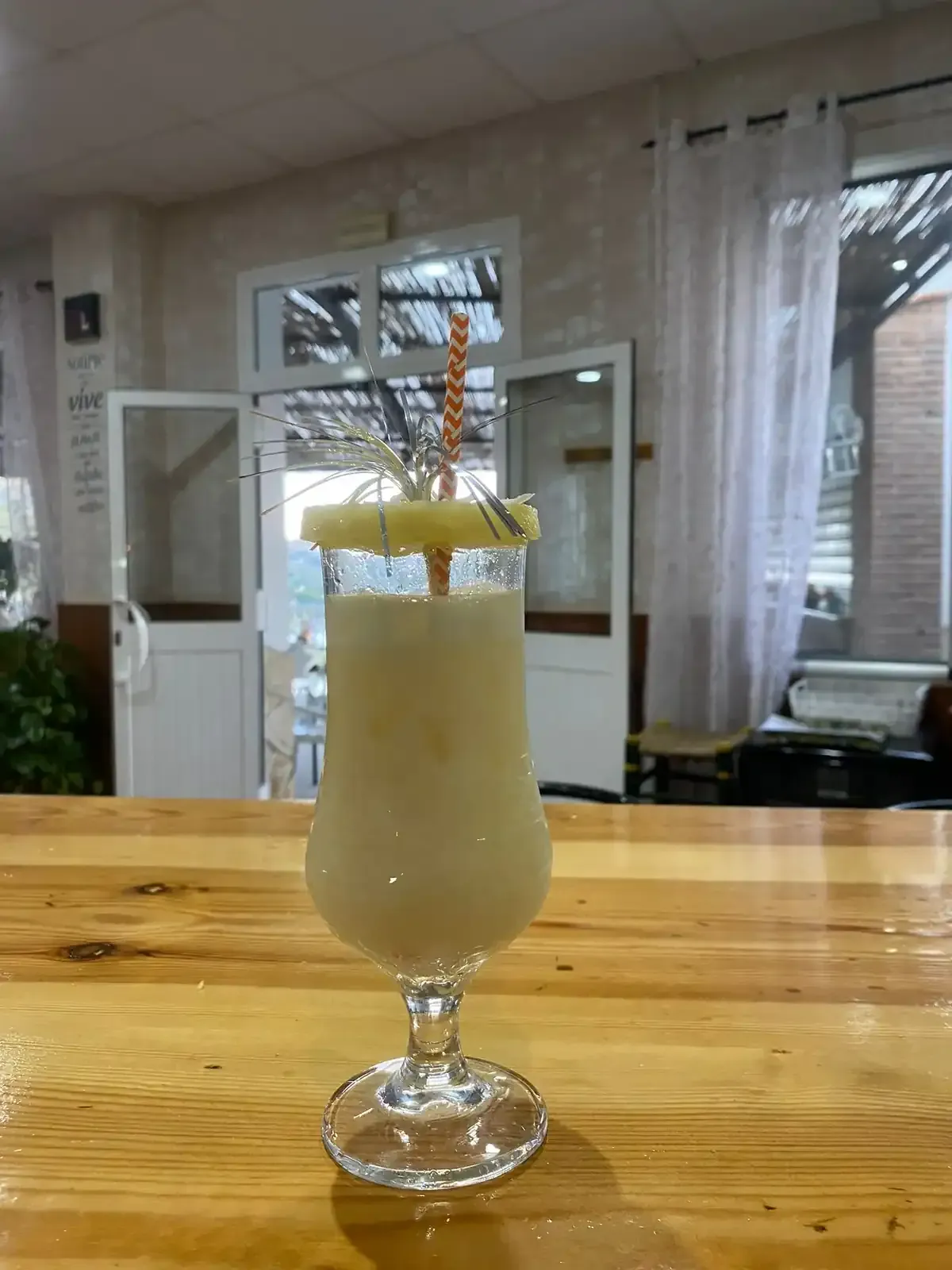 Cóctel de piña colada en vaso alto sobre barra de madera, adornado con piña y paja.