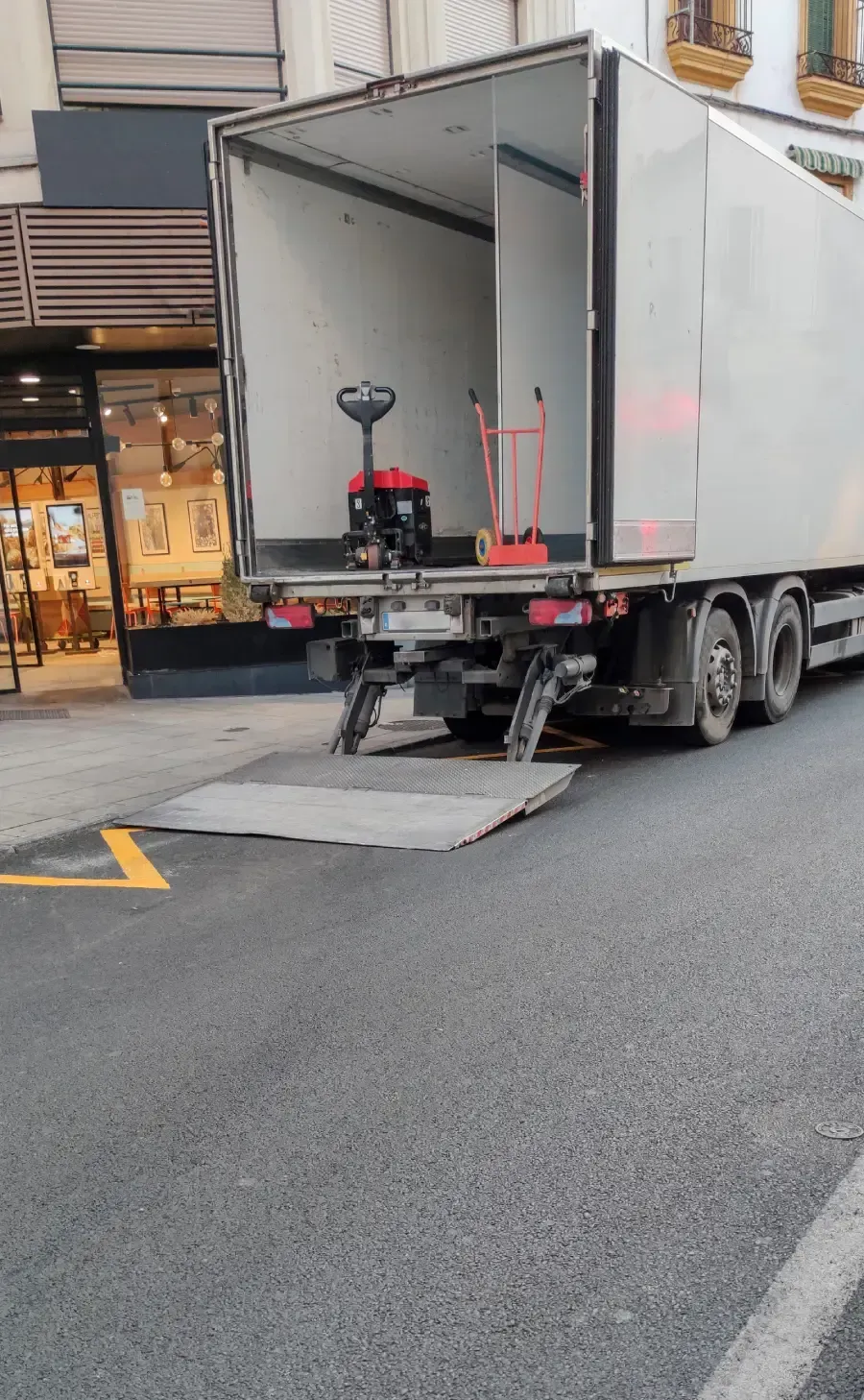 Camión de reparto con parte trasera abierta y rampa extendida en una calle de la ciudad.