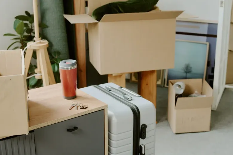Cajas y equipaje en la habitación, en movimiento. Una taza de viaje roja sobre una cómoda.