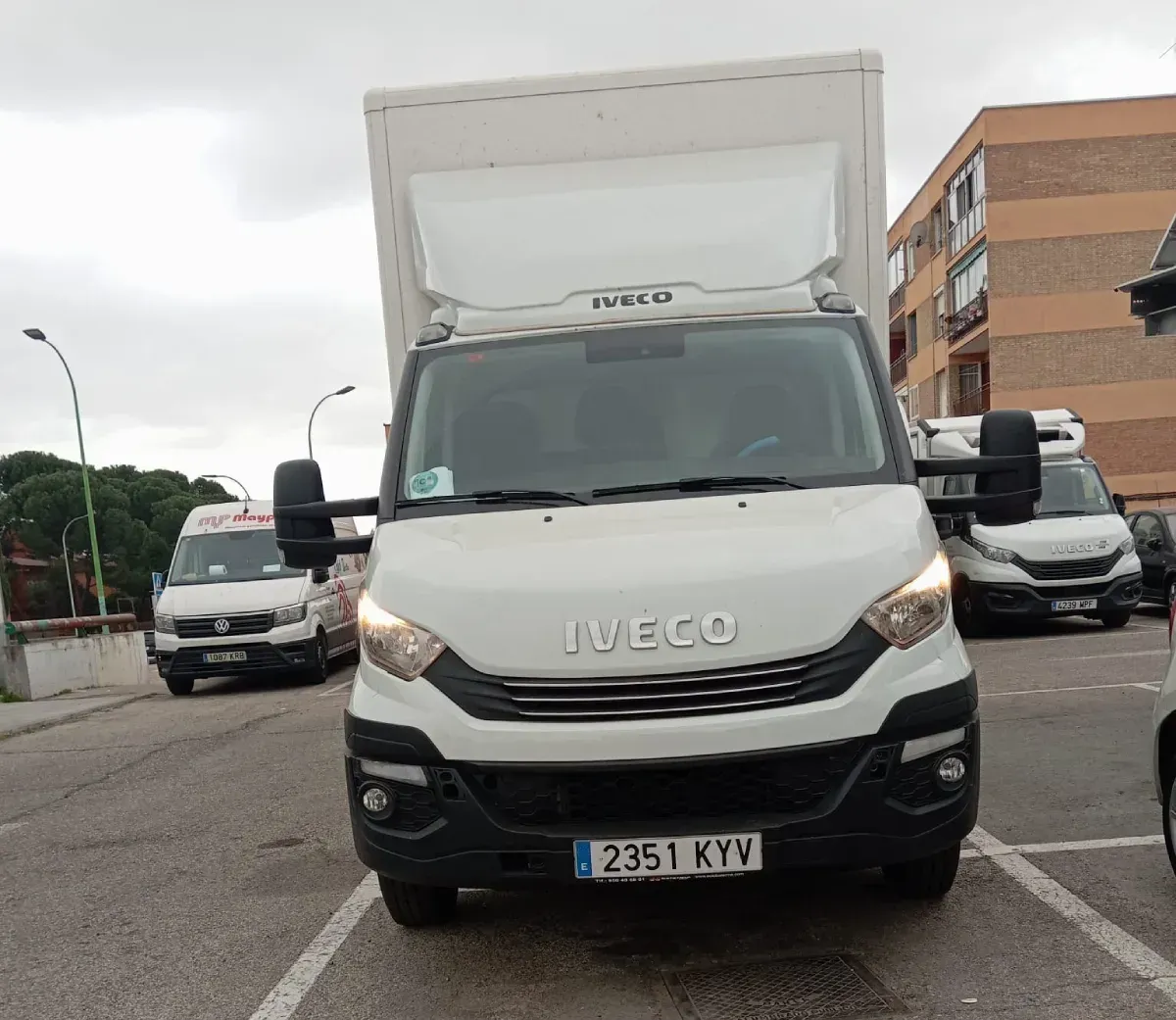 Camión de reparto Iveco blanco estacionado al aire libre con un edificio de la ciudad al fondo.