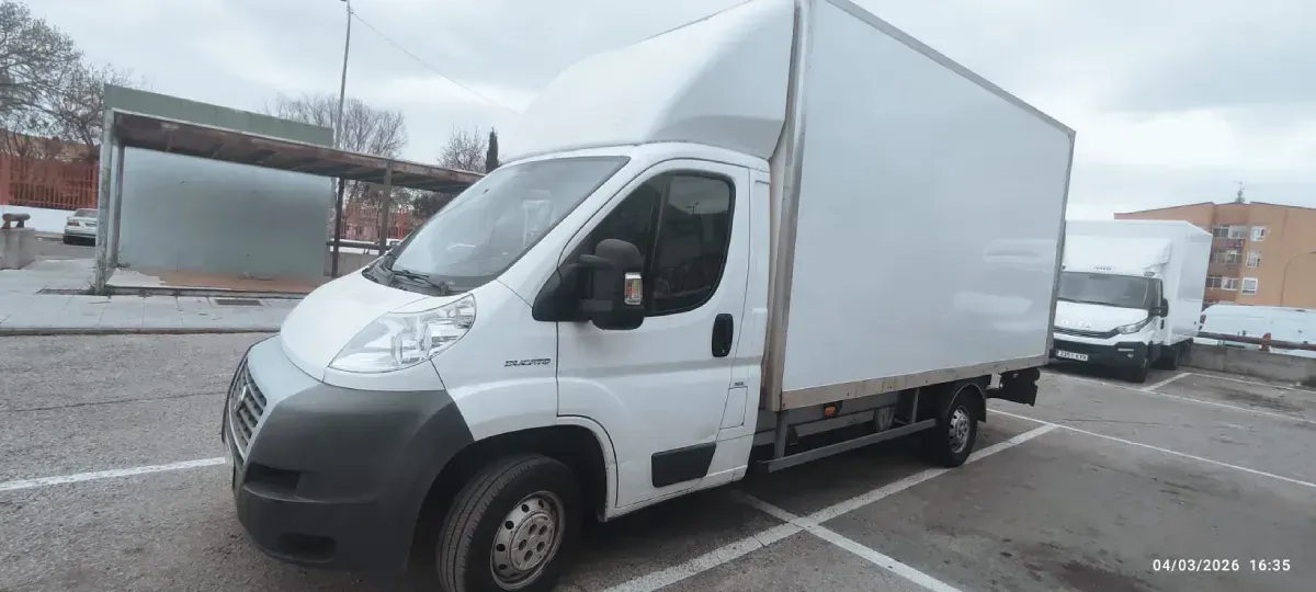 Una furgoneta de carga blanca estacionada en un estacionamiento en un día nublado.