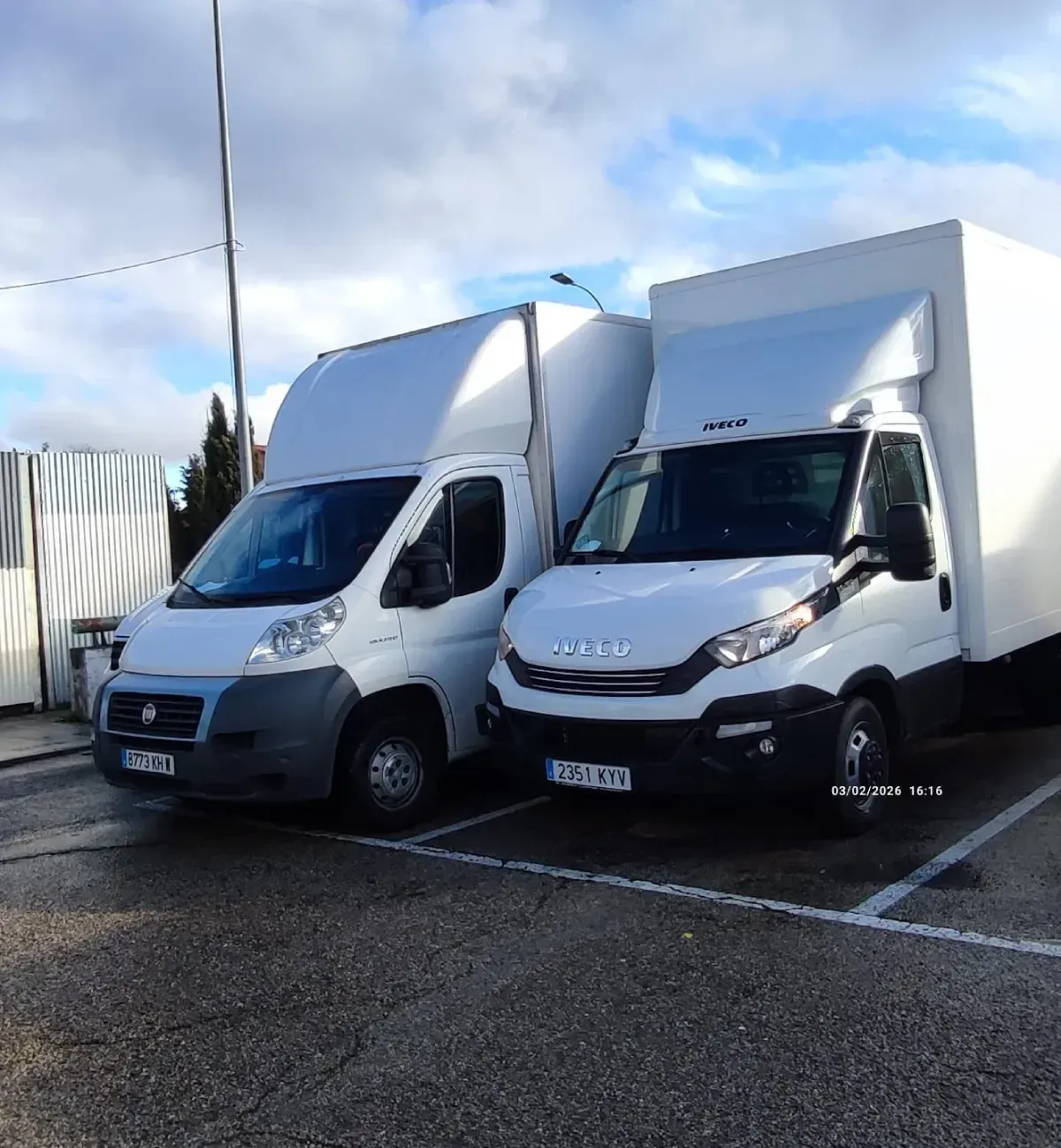 Dos furgonetas blancas de reparto estacionadas sobre el asfalto. Una es Fiat y la otra, Iveco. Cielo nublado al fondo.
