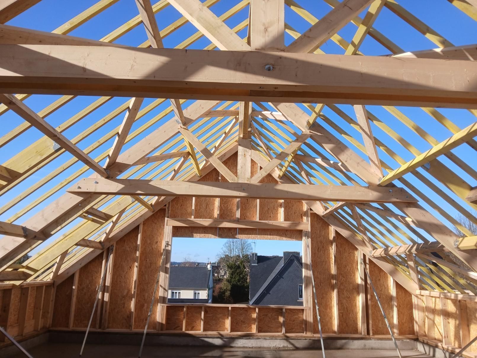 Vue de l'intérieur d'un grenier en construction, montrant les chevrons de charpente apparents et une grande ouverture de fenêtre.
