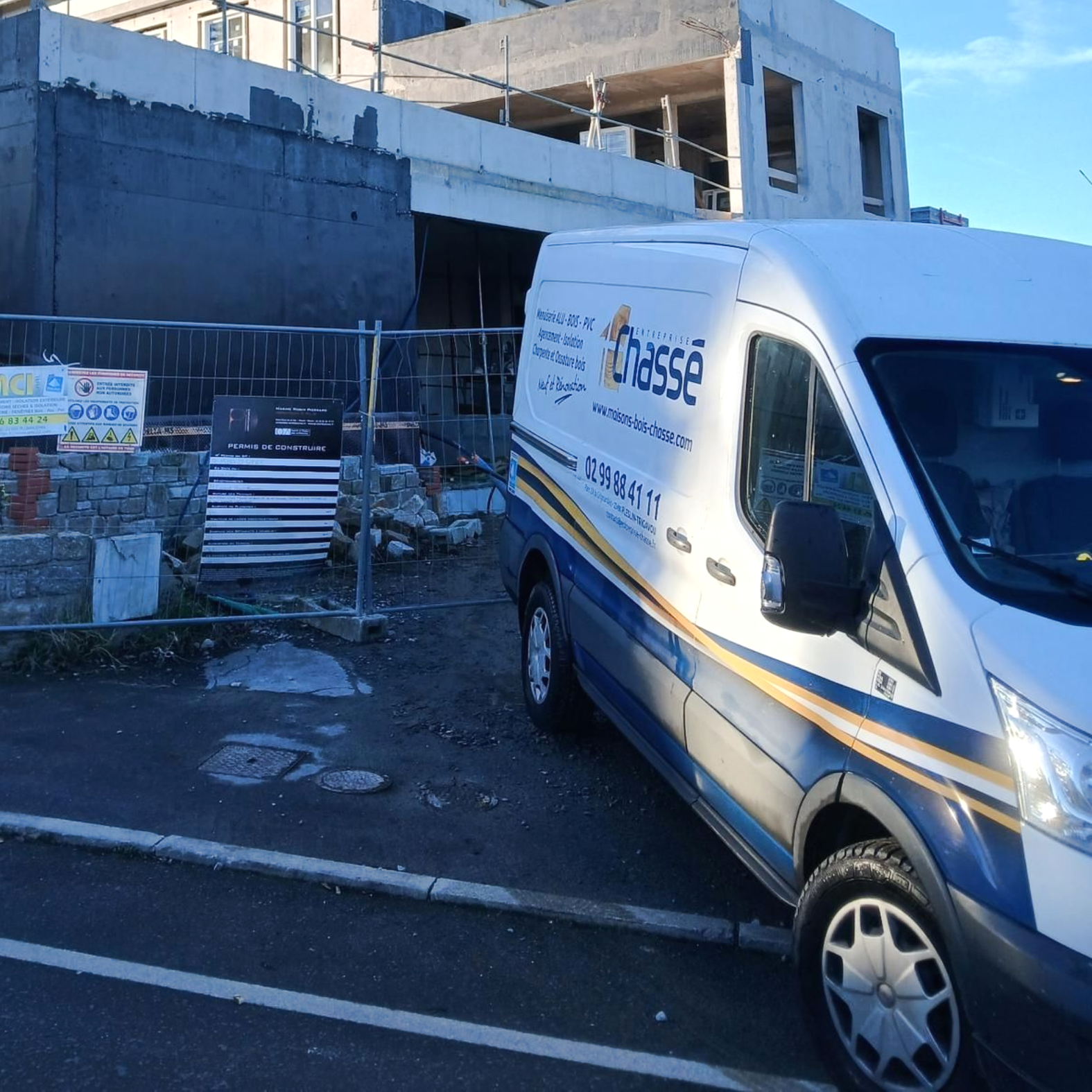 Une camionnette blanche de chantier avec le logo Chassé garée à côté d'un chantier clôturé, sous un ciel bleu azur.