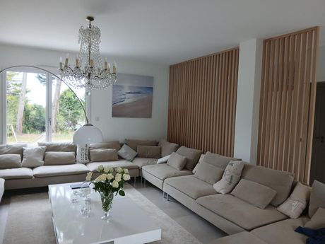 Un salon aux tons neutres avec un grand canapé d'angle beige en forme de L, une table basse blanche et des murs lambrissés de bois.