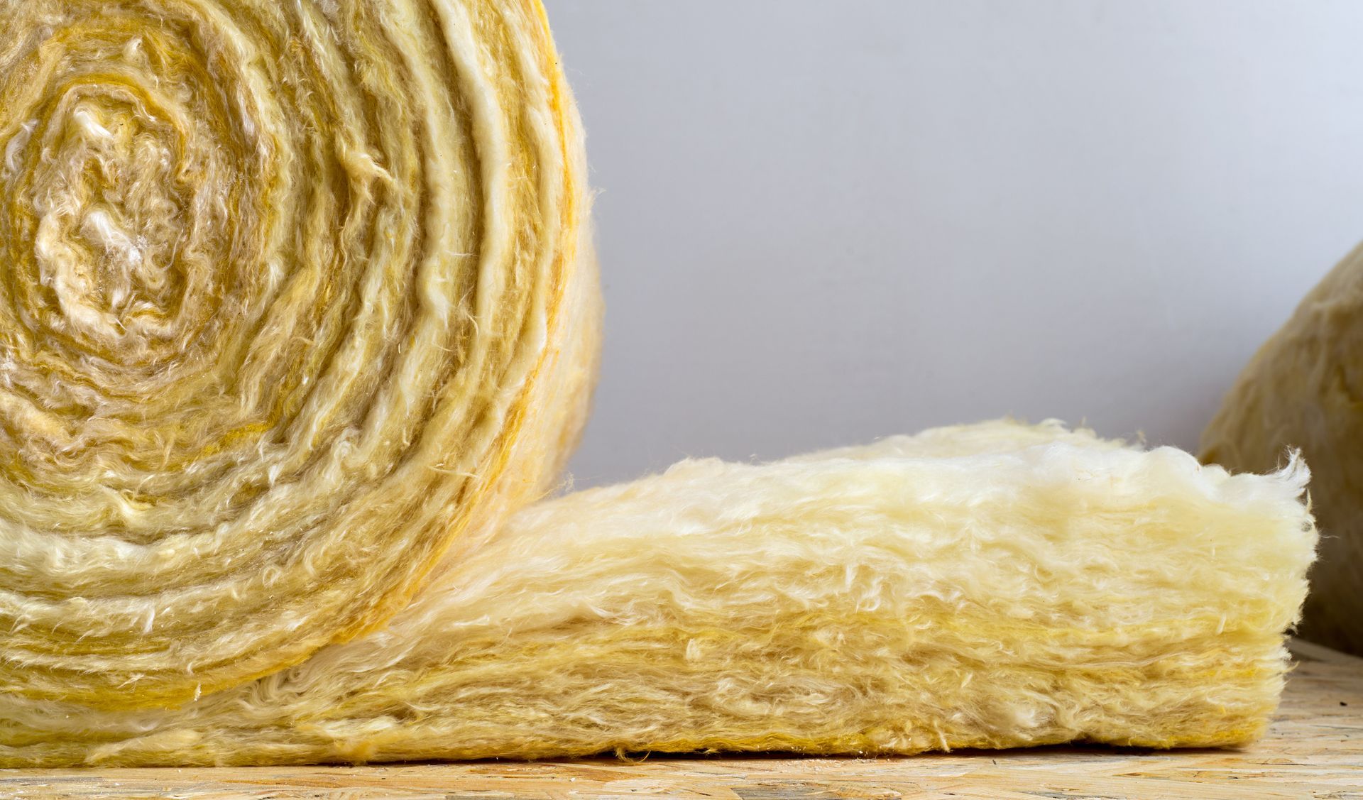 Un rouleau d'isolant en fibre de verre jaune, dont une section plate est déroulée pour montrer sa texture épaisse et fibreuse.