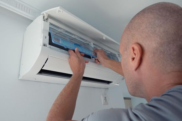 Persona limpiando el filtro de un aire acondicionado de pared en el interior