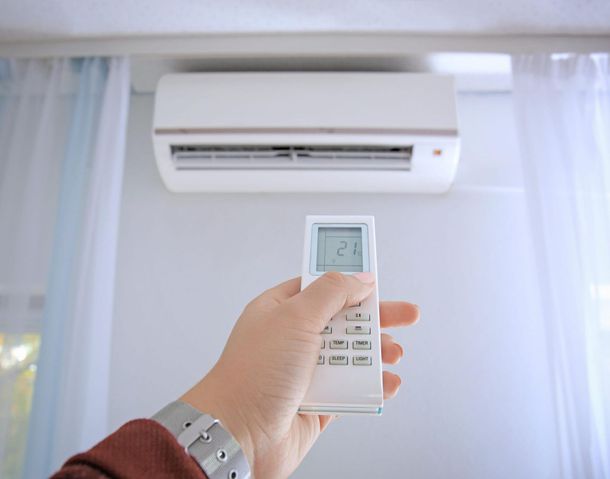 Una mano sostiene un mando a distancia apuntando a un aire acondicionado montado en la pared de una habitación luminosa