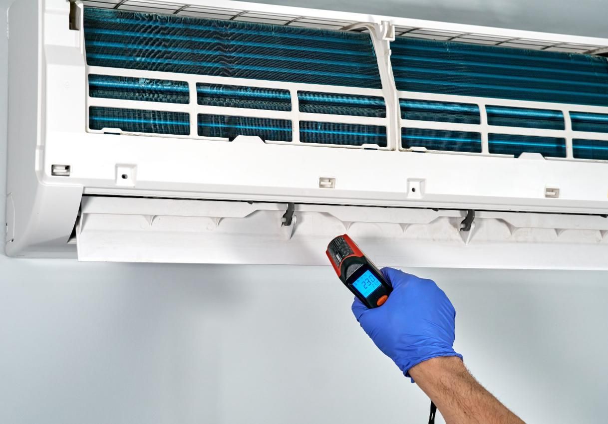 Una mano enguantada rocía desinfectante sobre el filtro de un aire acondicionado de pared.