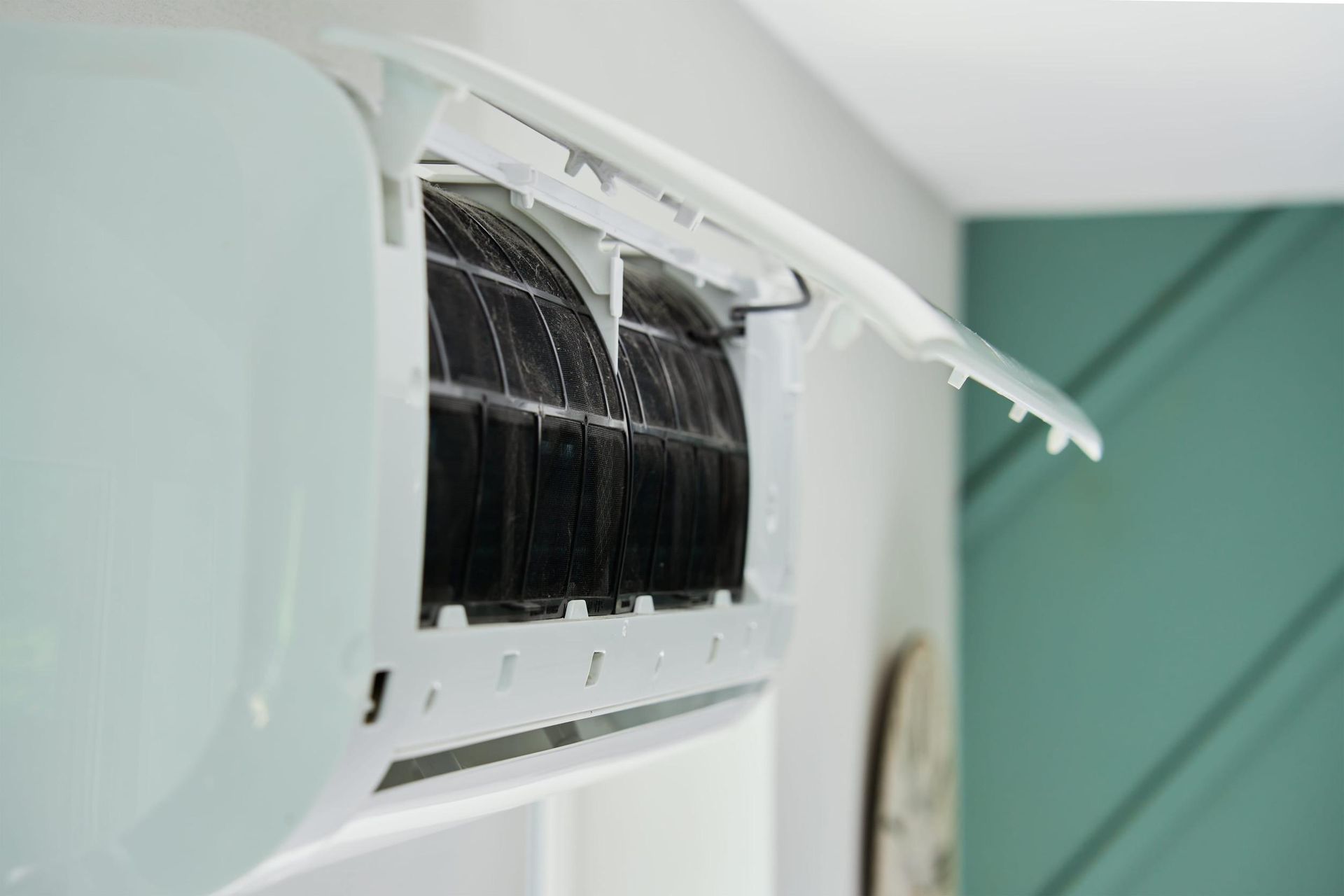 Rejilla del aire acondicionado abierta, con filtro negro y gotas de agua en el interior de una habitación