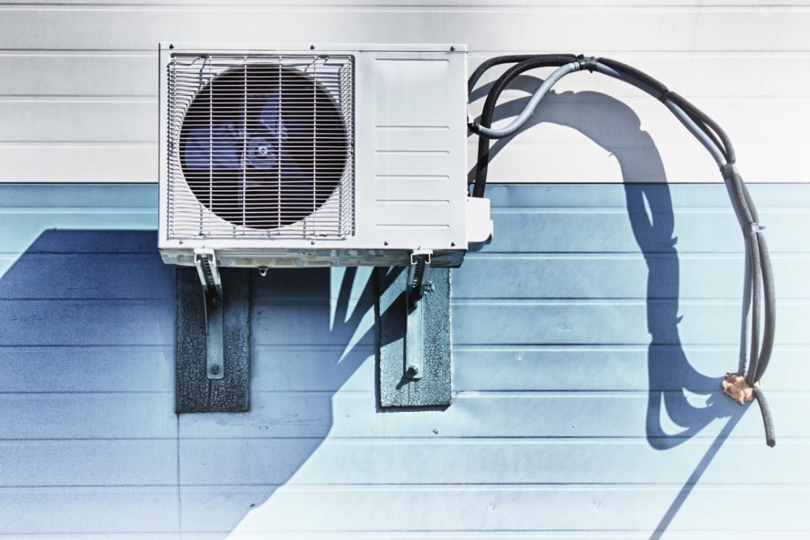 Unidad exterior del aire acondicionado instalada en una pared revestida de azul, con el conducto eléctrico