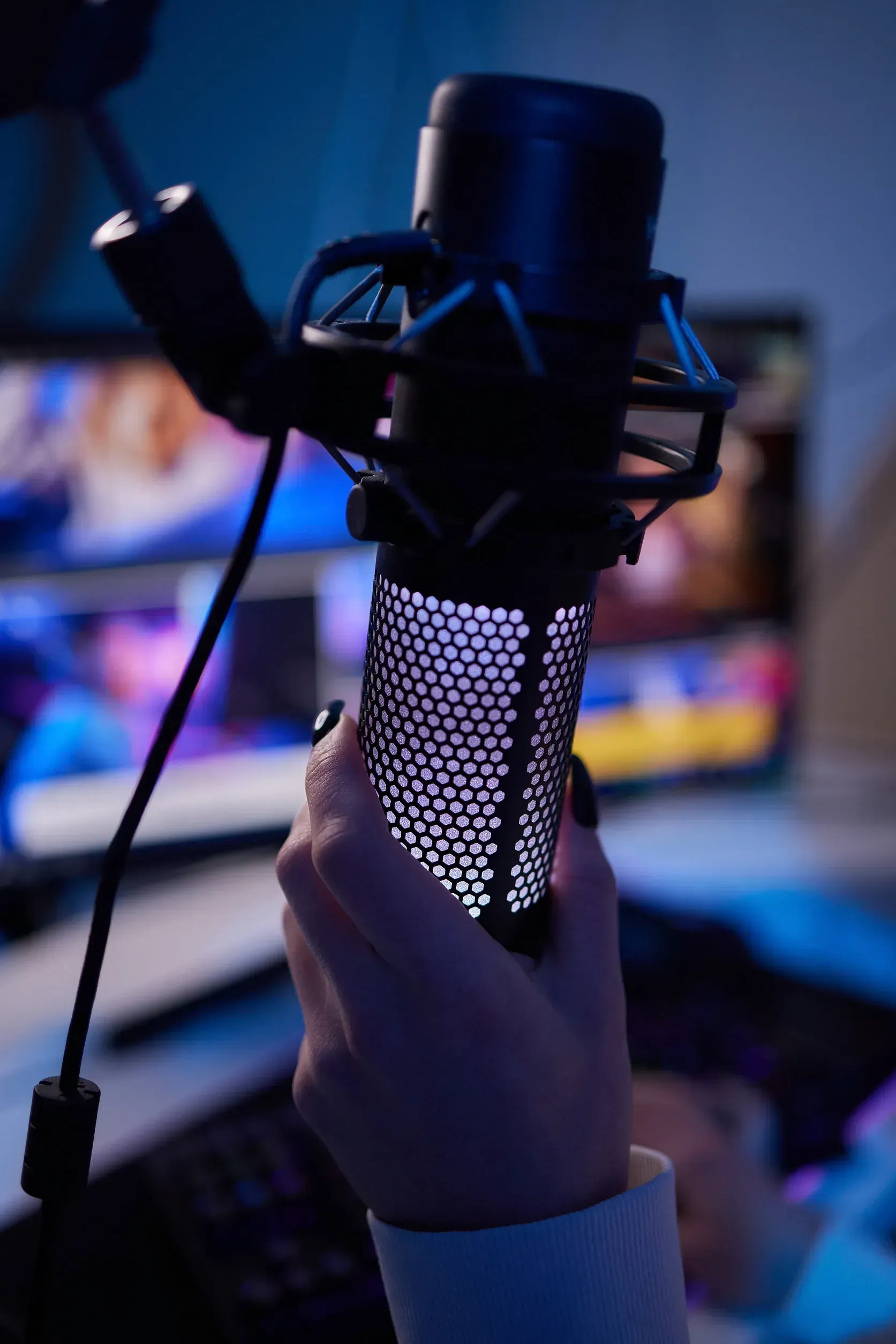 Una persona sostiene un micrófono negro con un patrón morado brillante. El micrófono está frente a una pantalla de computadora.
