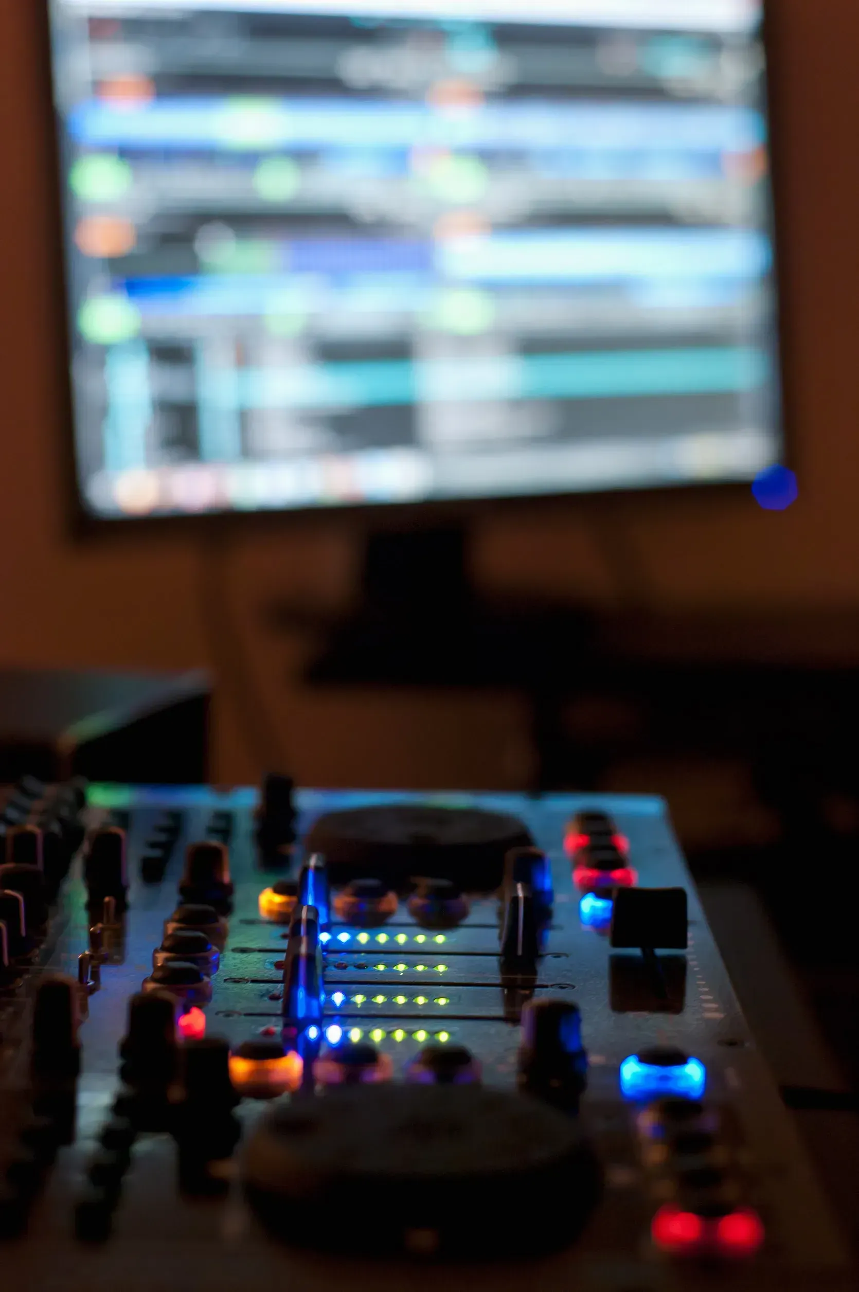 Consola de mezclas de DJ con faders iluminados, frente a una pantalla de computadora que muestra un software de música.