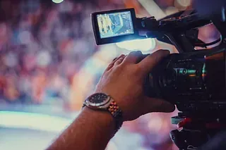 Persona que sostiene una cámara de vídeo, con reloj de pulsera visible, filmando un evento.