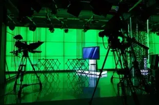 Estudio de televisión de pantalla verde con cámaras, luces y un monitor.