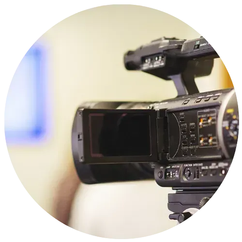 Se instala una cámara de vídeo profesional sobre un trípode, probablemente filmando un evento, con una pantalla de fondo.