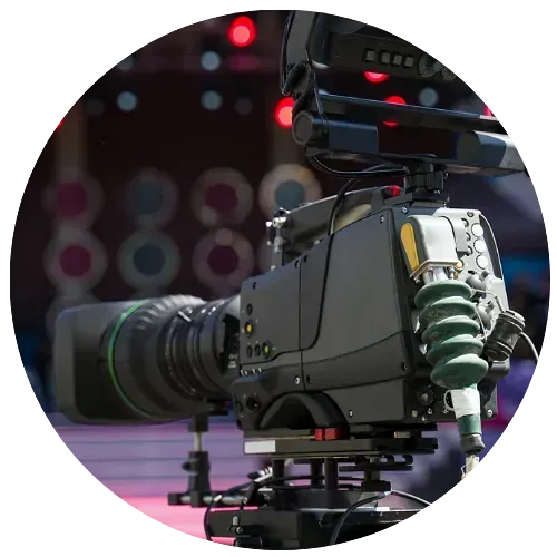 Primer plano de una cámara de vídeo profesional sobre un trípode, enfocando un fondo de escenario borroso con luces de colores.