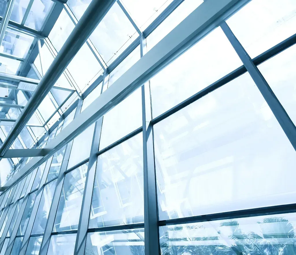 Ventanas de vidrio y techo de edificio moderno, vista en ángulo desde abajo, tonos azules y blancos.