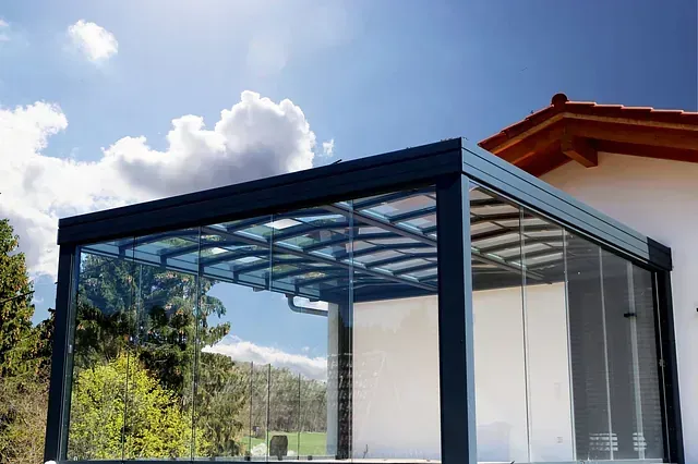 Moderno patio acristalado con marco negro adosado a una casa blanca bajo un cielo azul brillante.
