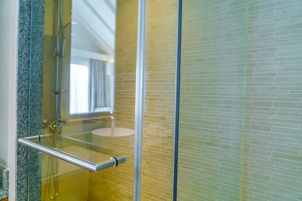 Mampara de ducha con puertas de cristal transparente y paredes alicatadas. Barra de acero inoxidable montada en el interior.