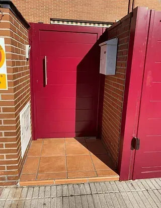 Puerta roja y buzón en una pared de ladrillo. Una pequeña entrada de azulejos conduce a la puerta.