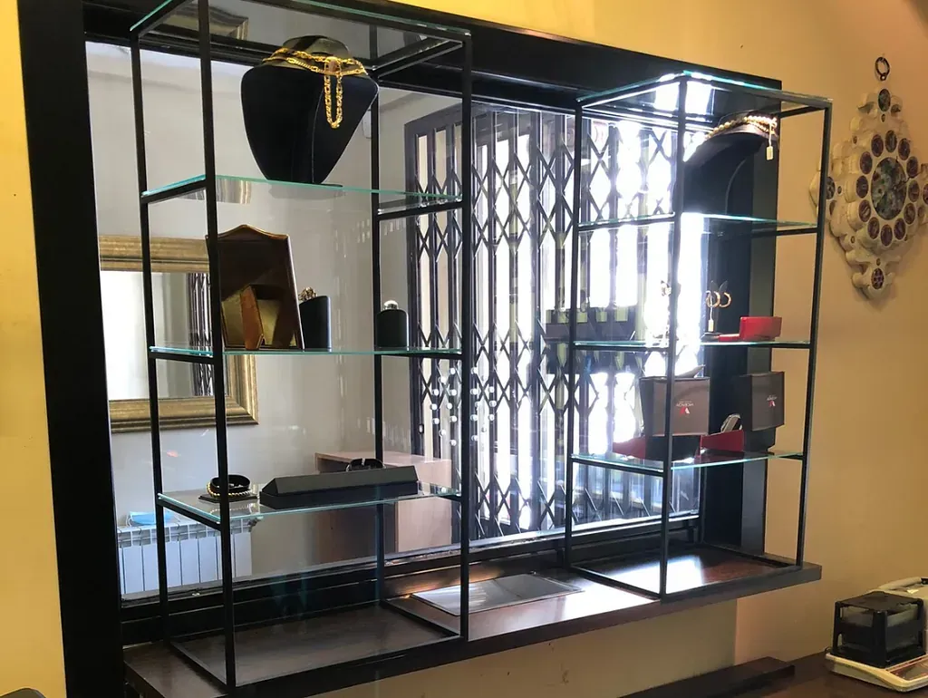 Vitrina con joyas sobre estantes de cristal, situada frente a una ventana con puerta de seguridad cerrada.