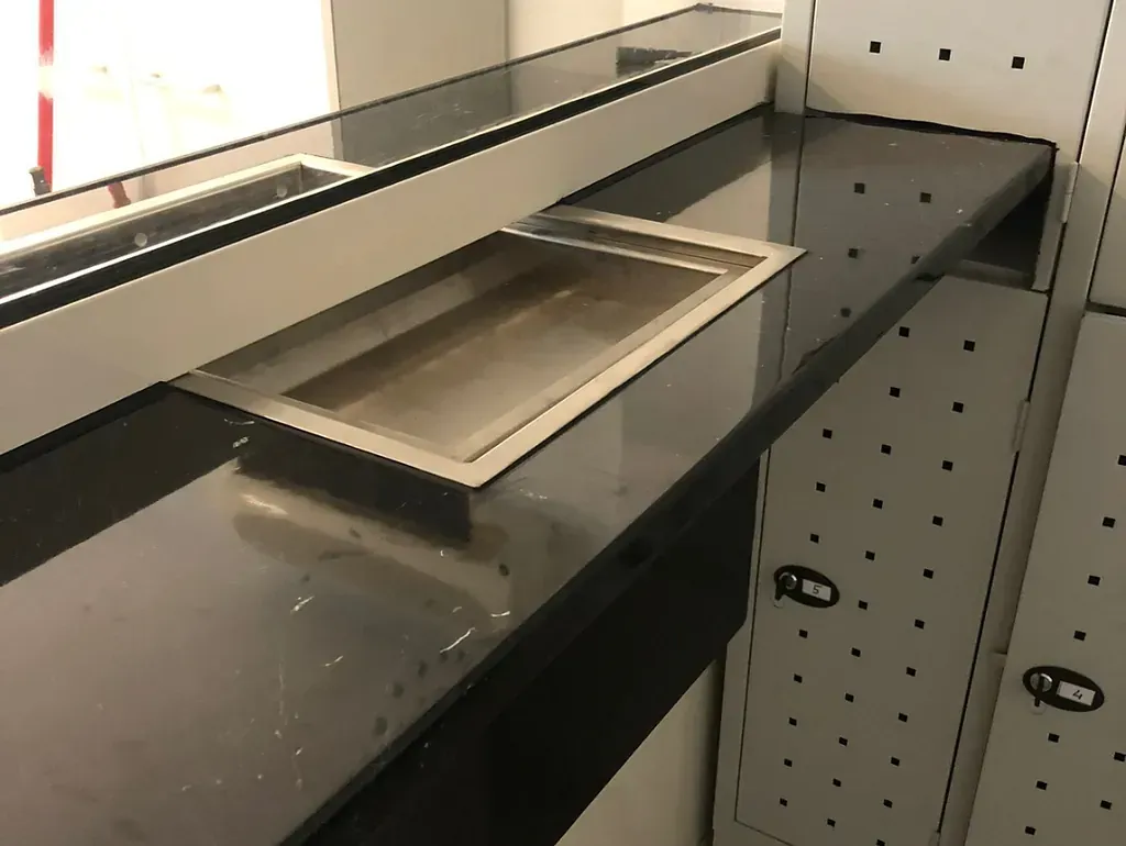 Una encimera negra con fregadero de acero inoxidable integrado. Forma parte de una estructura empotrada en una habitación bien iluminada.