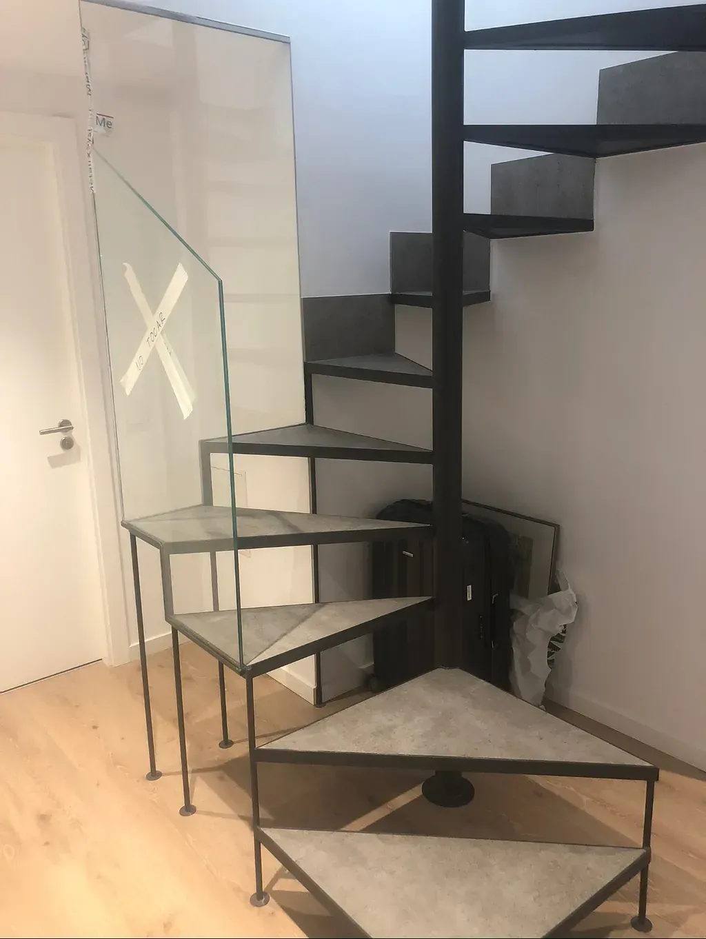 Una escalera de caracol de metal negro con escalones triangulares de hormigón. Tiene un panel de vidrio con una 