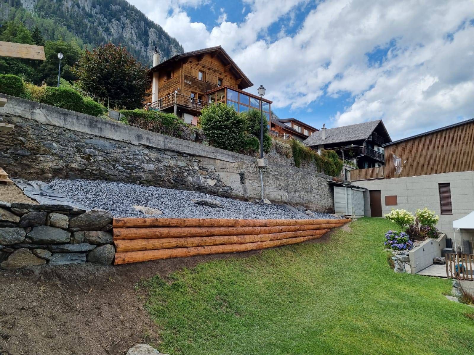 Un mur de soutènement en bois est en cours de construction devant une maison.