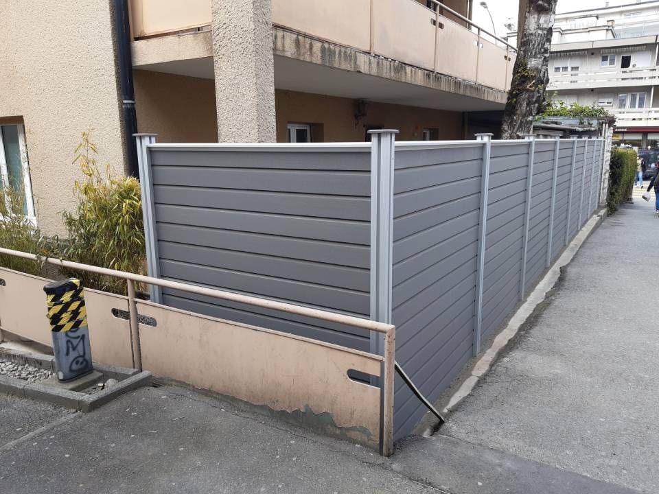 Une clôture grise se trouve sur le côté d'une rue à côté d'un bâtiment.