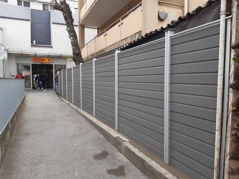 Une clôture grise le long d'un trottoir devant un bâtiment