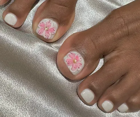 Un primer plano de las uñas de los pies de una mujer con una flor rosa en ellas.