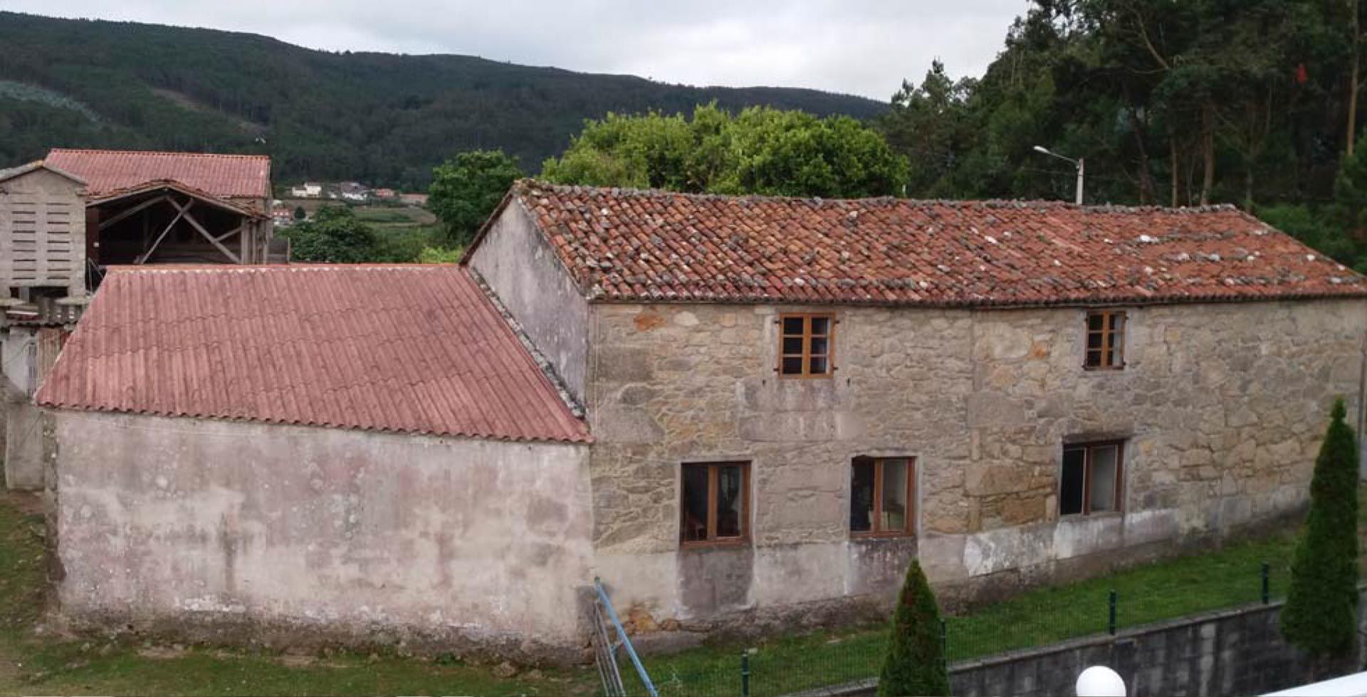 Un gran edificio de piedra con techo de tejas está rodeado de árboles y césped.