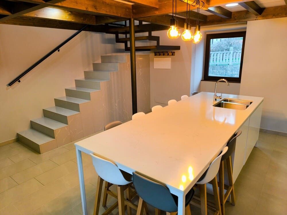 Una cocina con una larga mesa blanca y sillas y escaleras.