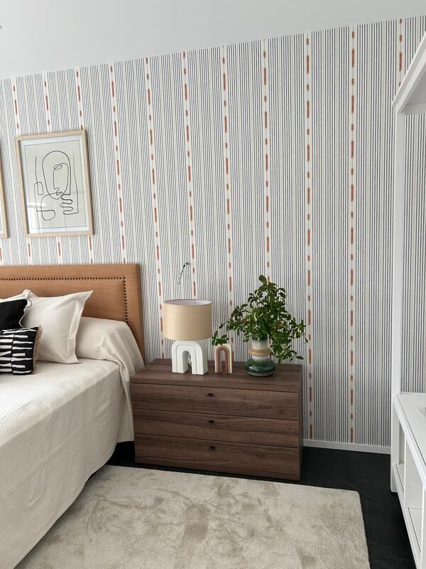 Un dormitorio con cama, mesita de noche, lámpara y papel pintado a rayas.