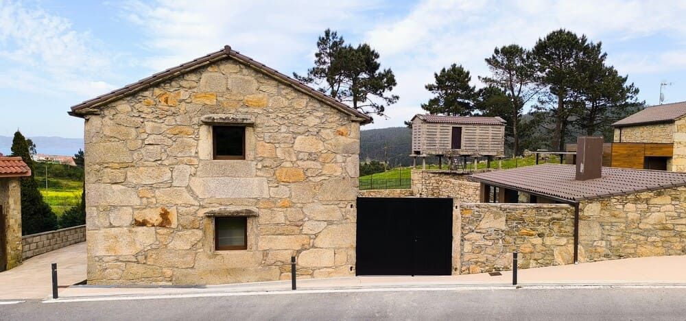 Una casa de piedra con una puerta de garaje negra está sentada al costado de la carretera.