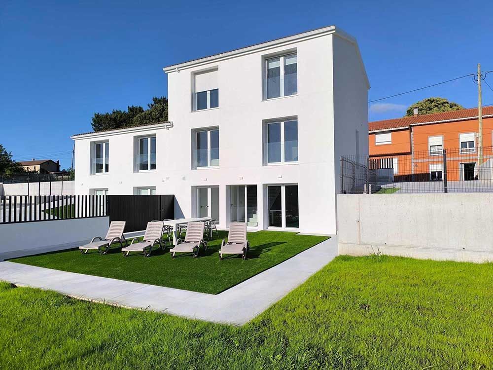 Una casa blanca con sillas de jardín delante de ella.