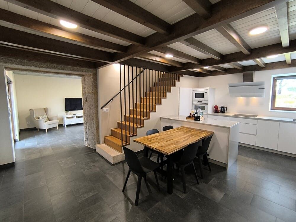 Una cocina con una mesa y sillas de madera y escaleras que conducen al segundo piso.