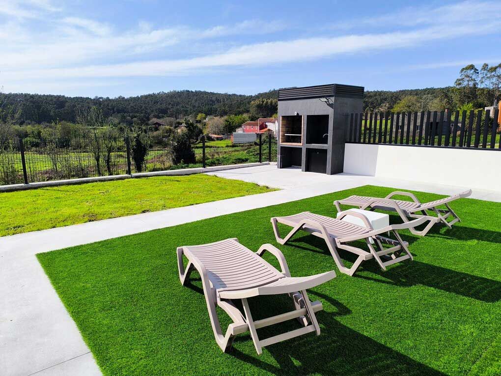 Un césped con sillas de jardín y una parrilla al fondo.