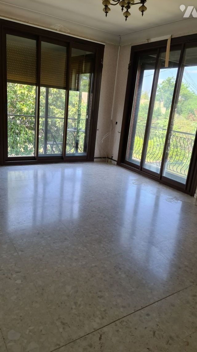 Pièce vide avec parquet ciré, grandes fenêtres et lumière du soleil inondant l'espace.