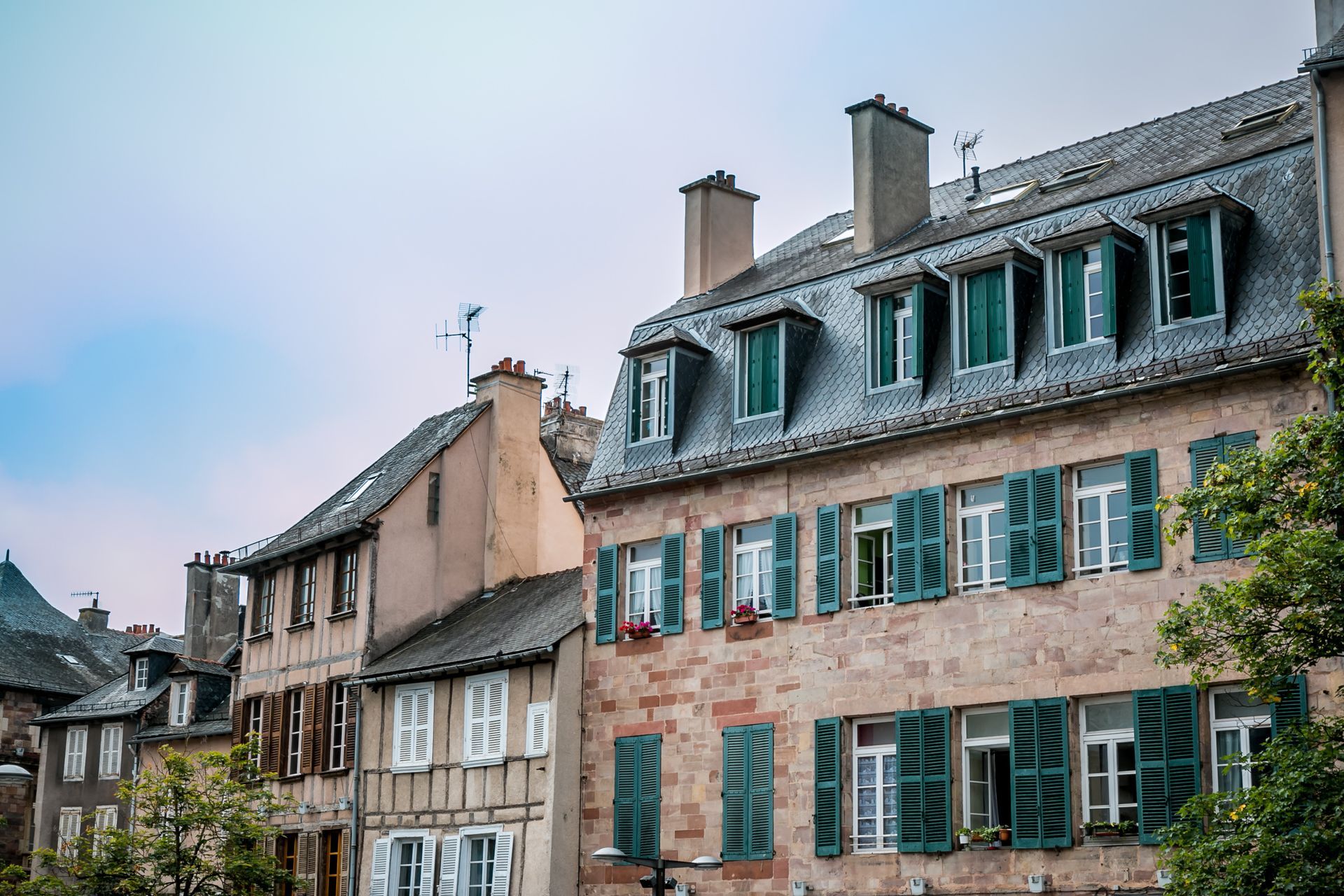 Des bâtiments aux volets verts et aux lucarnes sous un ciel nuageux.